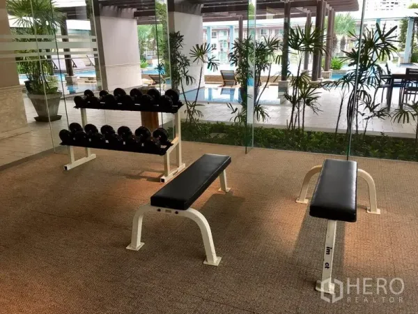 Condominium for rent in Khlong Toei, Bangkok - Fitness room with free weights and benches overlooking the pool through glass walls.