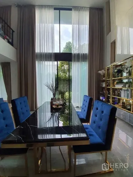 联排别墅 出售在Lat Phrao, Bangkok - 餐区配黑色大理石餐桌、蓝色软包椅，落地窗采光充足。