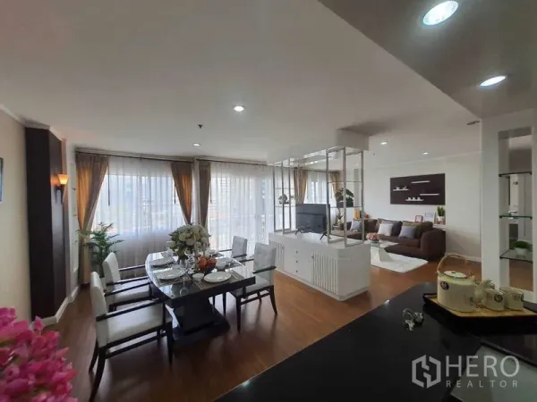 Apartment for rent in Watthana, Bangkok - Open-plan view from kitchen showing dining table, TV partition, and living area with full-height windows.