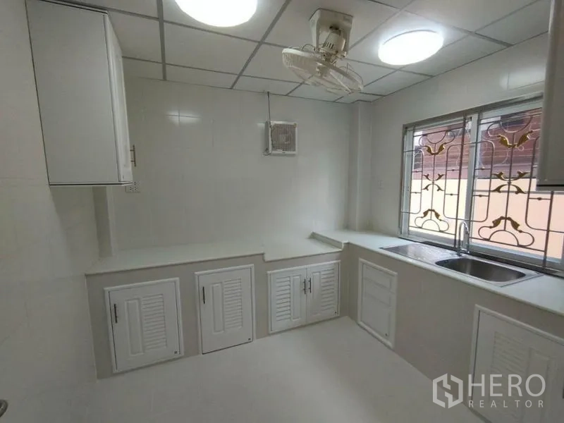 Detached House for rent in Khlong Toei, Bangkok - Spacious kitchen with L-shaped counters, ceiling fan and ventilation window.