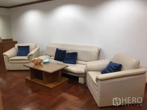 公寓 出租在Watthana, Bangkok - 明亮客厅配米色皮沙发、木质茶几和拼花木地板。