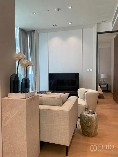 Condominium for rent in Pathum Wan, Bangkok - Cozy lounge with sofa, armchair, TV unit and tall curtains.