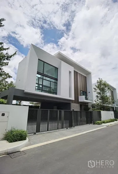 Detached House for rent or sale in Saphan Sung, Bangkok - Modern detached house facade with floor-to-ceiling windows, overhang roof and gated driveway on a quiet street.