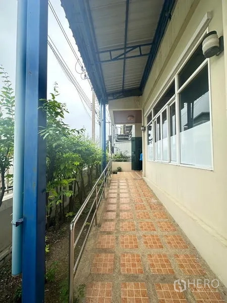 Warehouse for rent or sale in Lam Luk Ka, Pathum Thani - Tiled walkway with handrail along the side of the warehouse beneath a roof.