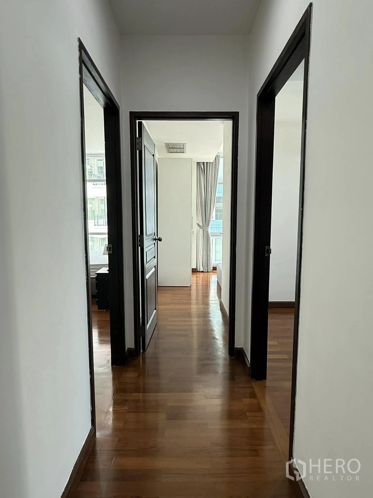 Condominium for rent in Pathum Wan, Bangkok - Hallway with wooden floors and doorways to multiple bedrooms.