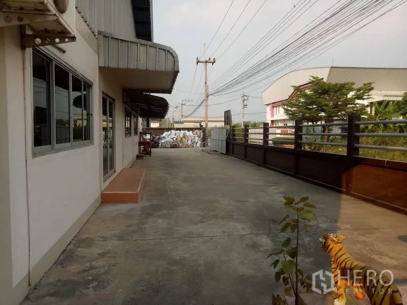 工厂 出租在Lat Lum Kaeo, Pathum Thani - 前院车道与办公室立面，旁有电线杆与邻近建筑。