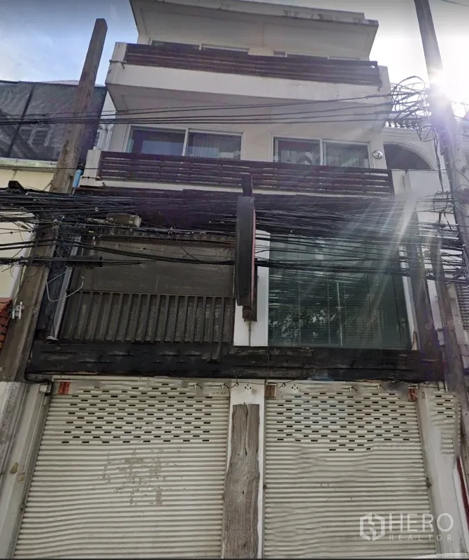 Shophouse for rent in Watthana, Bangkok - Multi-storey shophouse facade with balconies and closed roller shutters.