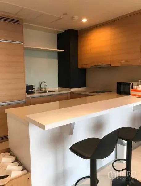 Condominium for sale in Khlong Toei, Bangkok - Open kitchen with light wood cabinets, white peninsula counter and bar stools.