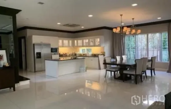 Detached House for sale in Bang Phli, Samut Prakan - Open-plan dining area beside a modern island kitchen with white cabinetry, stainless refrigerator, and large windows.