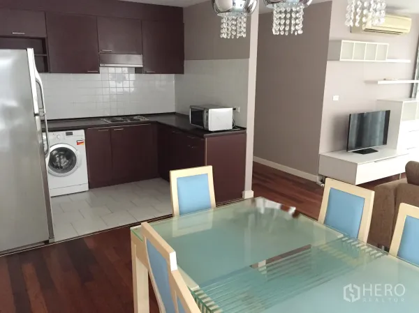 Condominium for rent in Watthana, Bangkok - Glass dining table for six facing an L-shaped kitchen with washer and TV console.