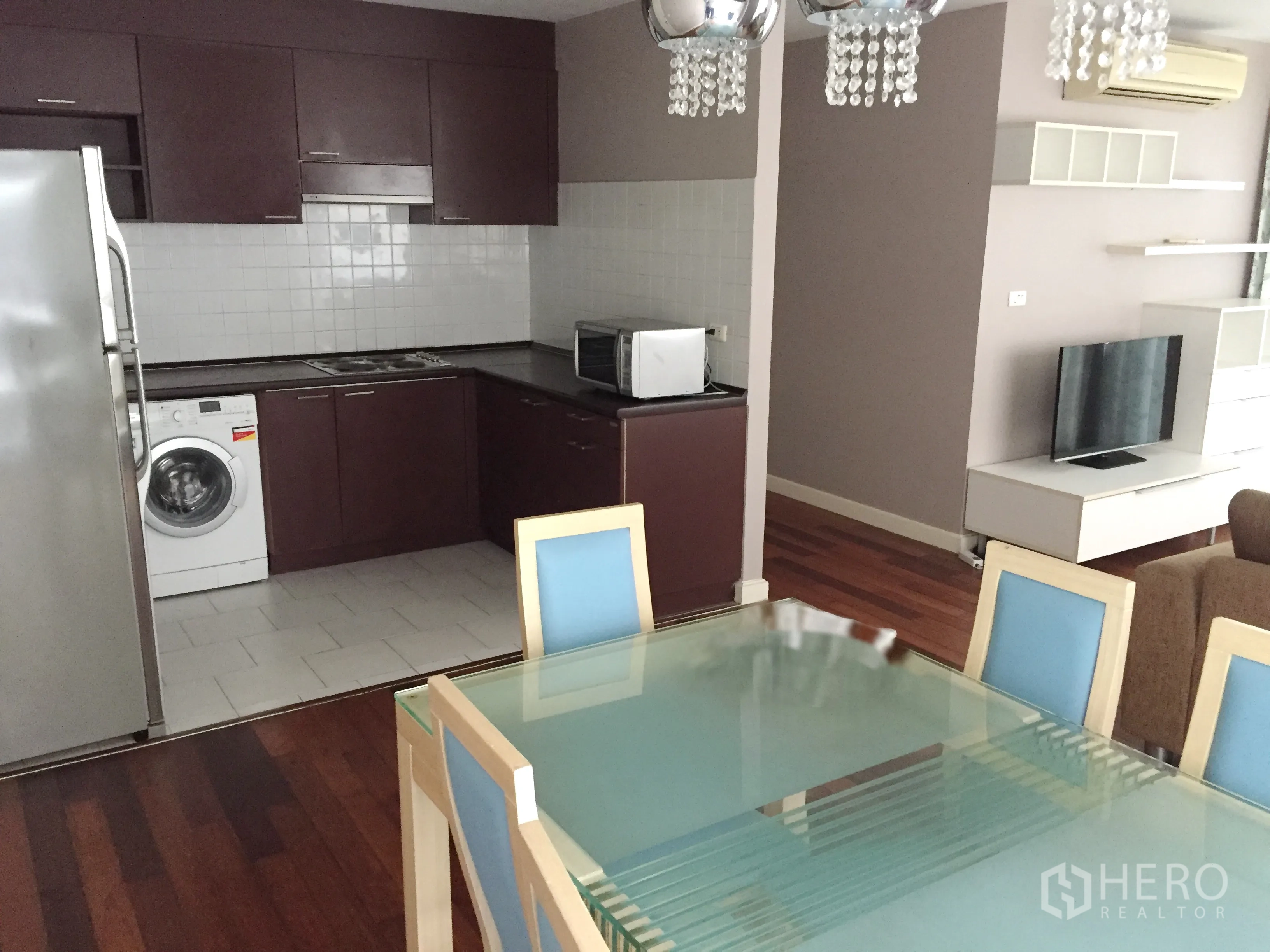 Condominium for rent in Watthana, Bangkok - Glass dining table for six facing an L-shaped kitchen with washer and TV console.