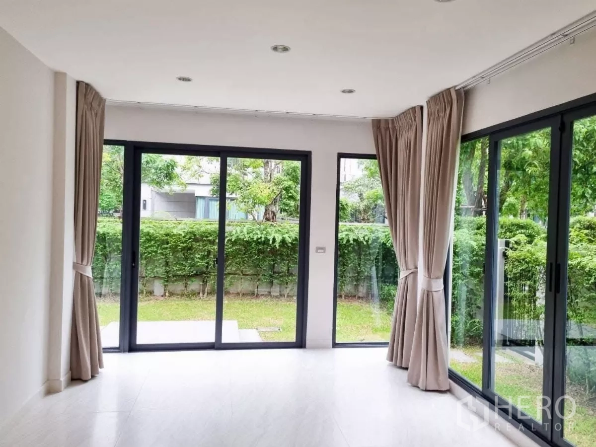 独立式住宅 出售在Prawet, Bangkok - 玻璃墙起居区，推拉门望向绿篱花园。