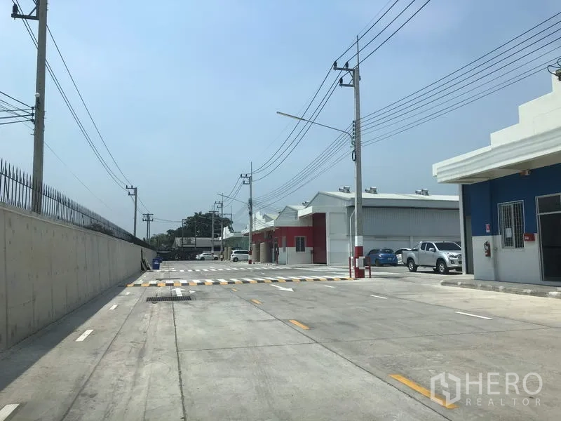 Factory for rent in Khlong Luang, Pathum Thani - Wide internal road of the industrial compound with security fencing and utility poles.