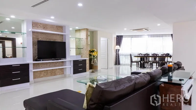 Condominium for rent or sale in Khlong Toei, Bangkok - Spacious living area with TV feature wall, glass shelves and view to dining zone.