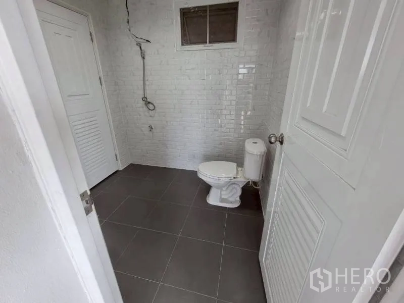 Warehouse for rent in Lam Luk Ka, Pathum Thani - Clean restroom with toilet, handheld shower, tiled floor, and small window.