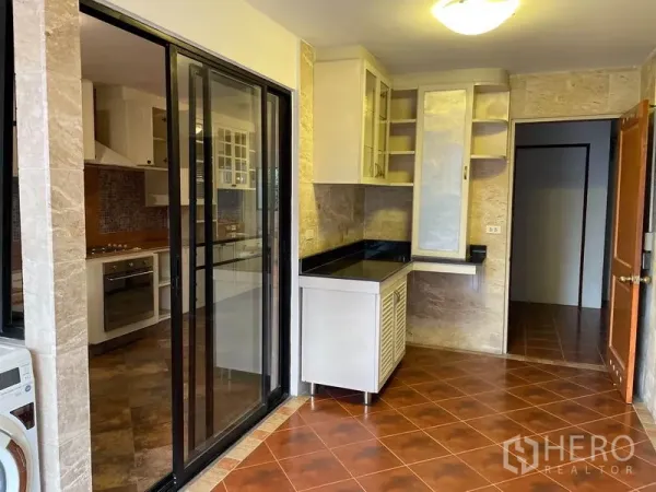 Condominium for rent in Watthana, Bangkok - Glass sliding door separates utility area and modern kitchen with stone walls and black countertops.