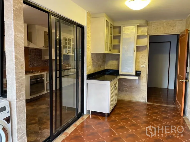 Condominium for rent in Watthana, Bangkok - Glass sliding door separates utility area and modern kitchen with stone walls and black countertops.