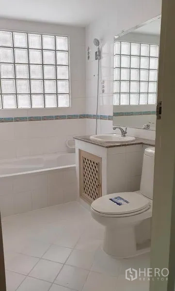 Townhouse for rent or sale in Chatuchak, Bangkok - White bathroom with glass-block window, built-in bathtub, vanity and toilet.