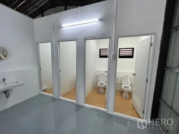 Warehouse for rent in Lat Phrao, Bangkok - Row of restroom cubicles with toilets, small windows and a wall-mounted sink.