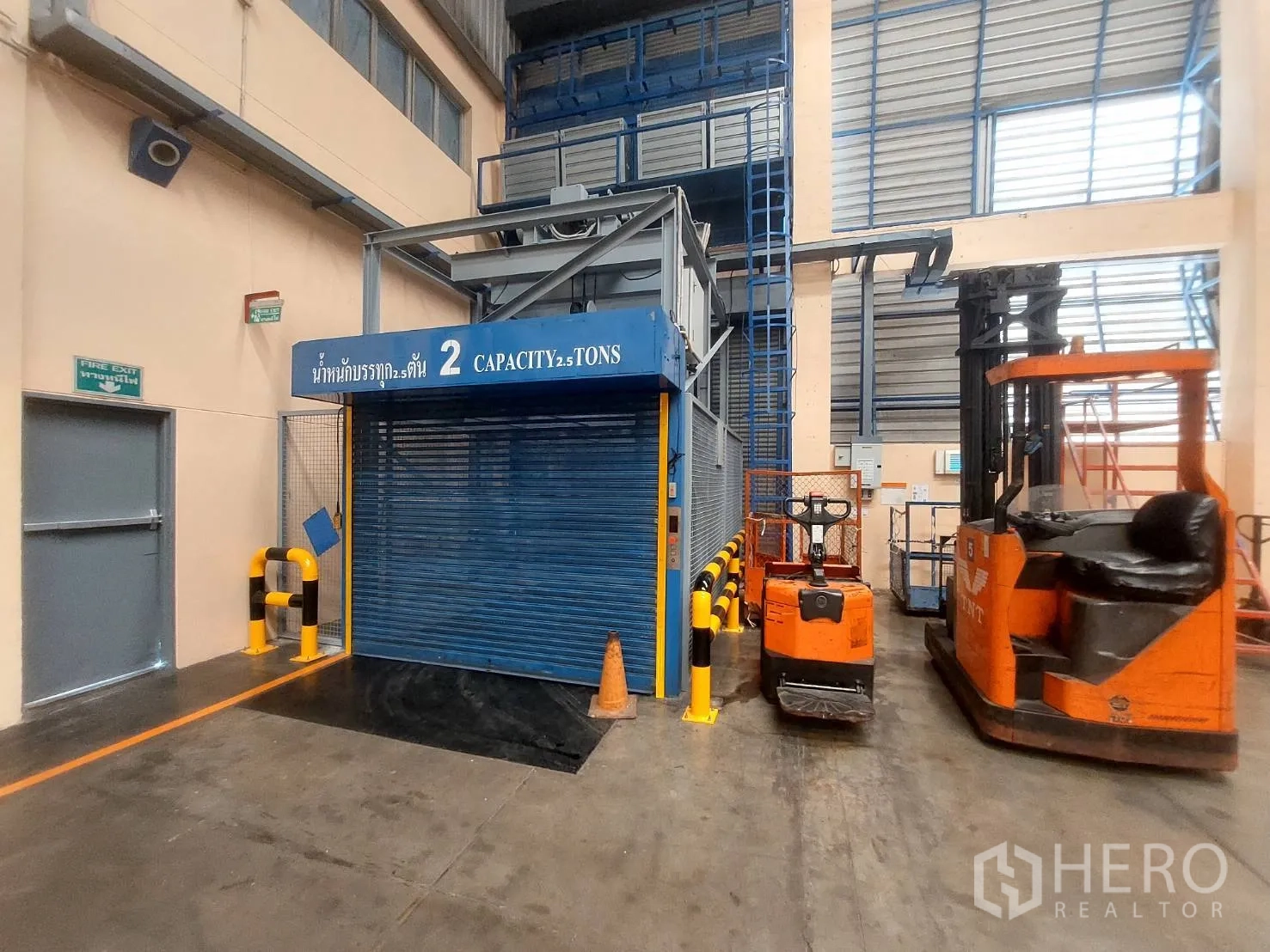 Warehouse for rent in Mueang Pathum Thani, Pathum Thani - 2.5-ton freight elevator beside forklifts and an emergency exit door.