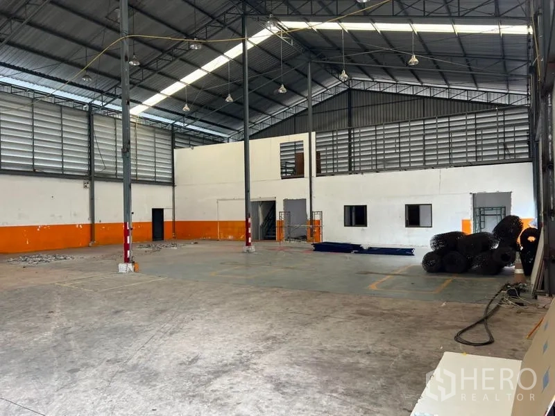 Warehouse for rent in Prawet, Bangkok - Spacious warehouse interior featuring high steel truss roof, skylights and louvered ventilation, concrete floor and built‑in office rooms.