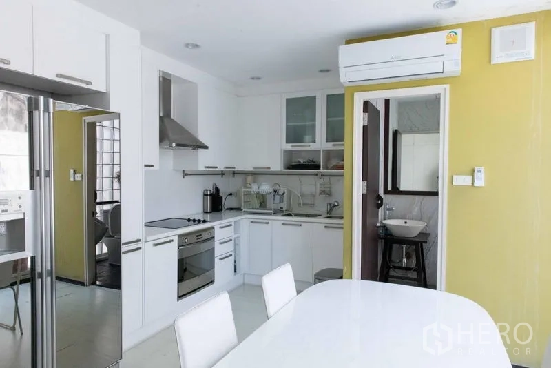 Townhouse for sale - Modern white kitchen with dining table, built‑in oven and doorway to a powder room.