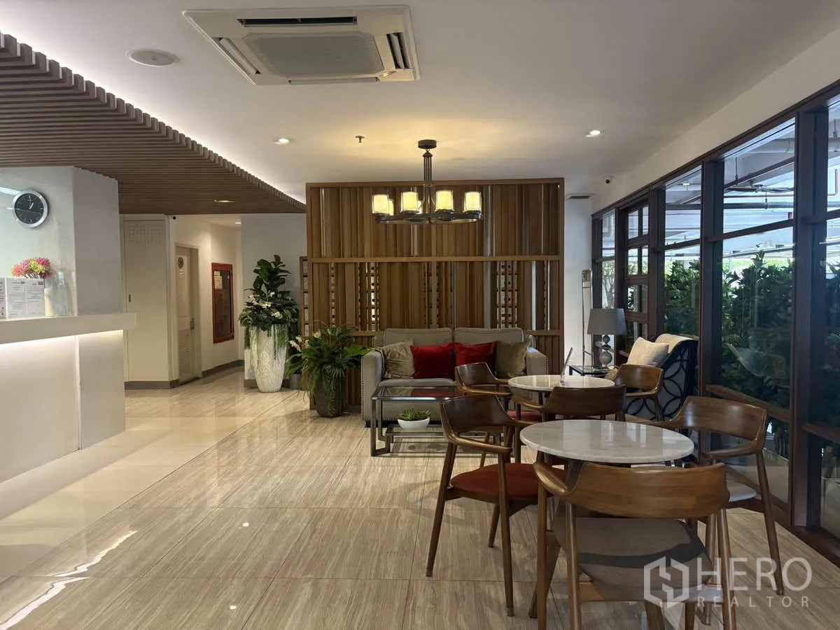 Condominium for rent in Khlong Toei, Bangkok - Modern residents’ lounge with reception counter and cafe‑style tables by large windows.