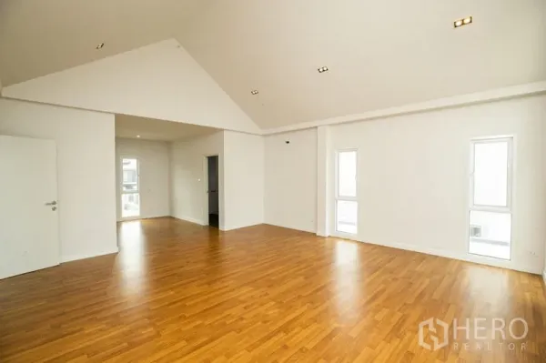 Detached House for rent or sale in Lam Luk Ka, Pathum Thani - Spacious open-plan room with pitched ceiling, recessed lights and wood flooring.