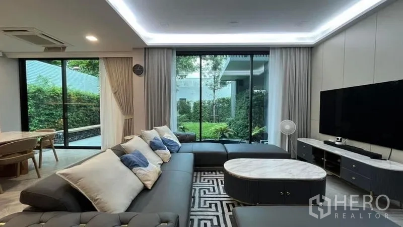 Detached House for sale in Saphan Sung, Bangkok - Bright living room featuring a large sectional sofa, TV wall and sliding doors opening to the garden.