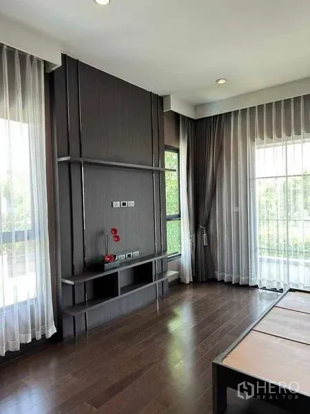 独立式住宅 出售在Prawet, Bangkok - 转角房间，深色木地板，电视背景墙与大窗。