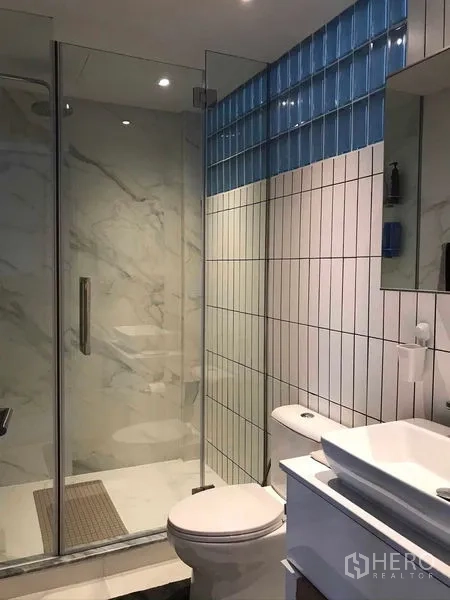 Townhouse for rent or sale in Khlong Toei, Bangkok - Contemporary bathroom with glass shower enclosure, marble‑look tiles and blue accent strip.