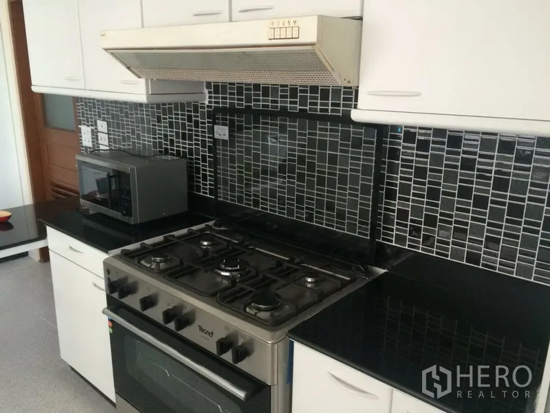 Condominium for rent in Khlong Toei, Bangkok - Modern kitchen with gas stove, range hood, black mosaic backsplash and white cabinetry.