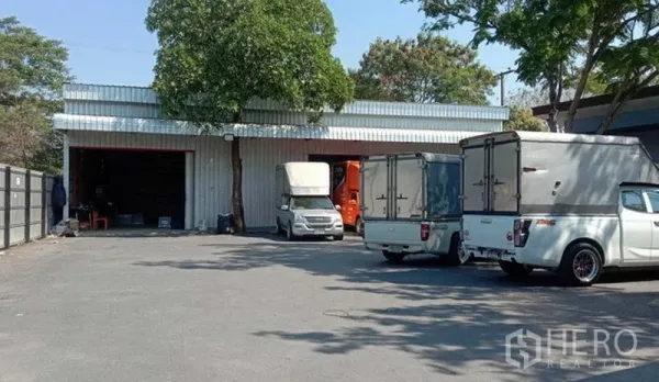 Warehouse for rent in Khlong Sam Wa, Bangkok - Front of warehouse with spacious driveway and parked box trucks, showing ample maneuvering space for logistics.