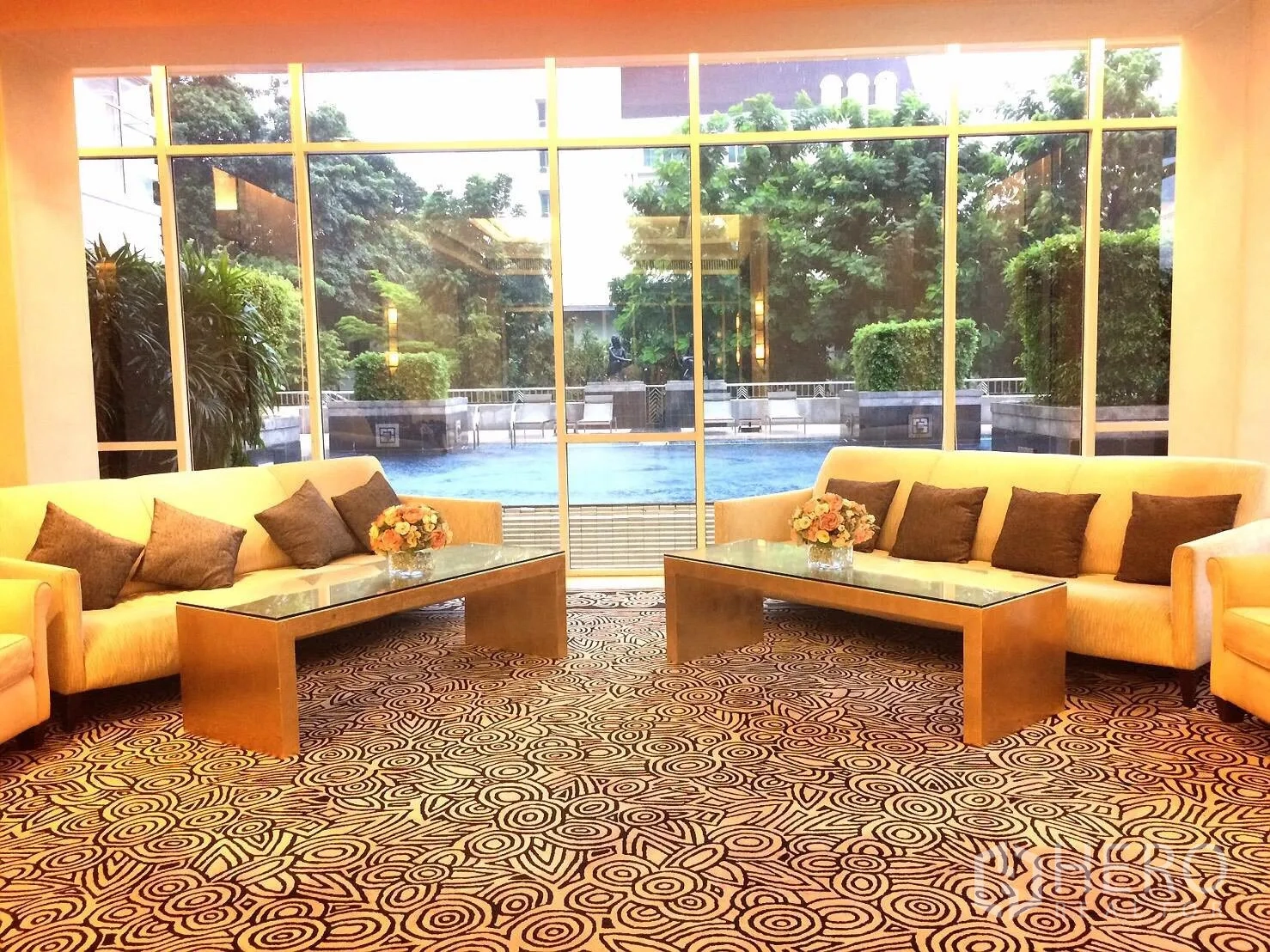 Condominium for rent in Watthana, Bangkok - Condo lounge with sofas and glass coffee tables facing an outdoor swimming pool and greenery.