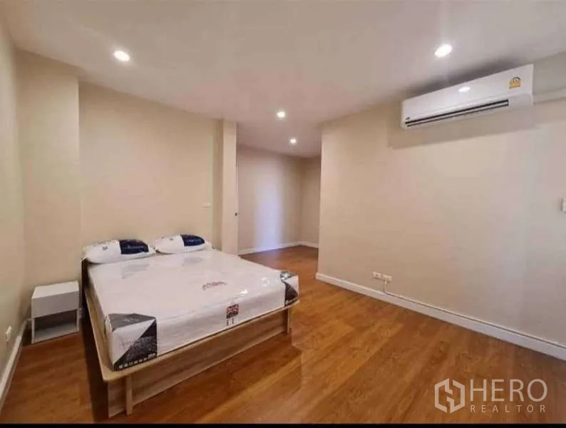 Townhouse for rent in Phra Khanong, Bangkok - Spacious bedroom with queen bed, wood flooring, recessed lights and wall-mounted air conditioner.