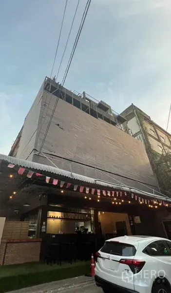 Shophouse for rent or sale in Watthana, Bangkok - Multi‑storey shophouse exterior with cafe‑style ground floor, awning and evening lights in an urban street.