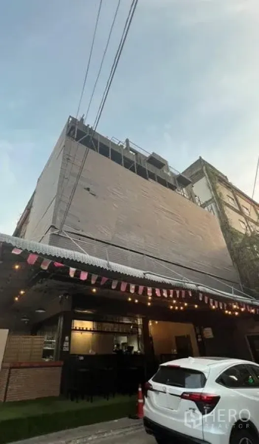 Shophouse for rent or sale in Watthana, Bangkok - Multi‑storey shophouse exterior with cafe‑style ground floor, awning and evening lights in an urban street.