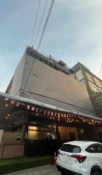Shophouse for rent or sale in Watthana, Bangkok - Multi‑storey shophouse exterior with cafe‑style ground floor, awning and evening lights in an urban street.