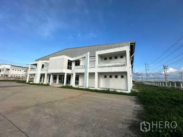 Factory for rent in Khlong Luang, Pathum Thani - Two-storey factory exterior in Khlong Luang with wide concrete yard and roadside power lines under a blue sky.