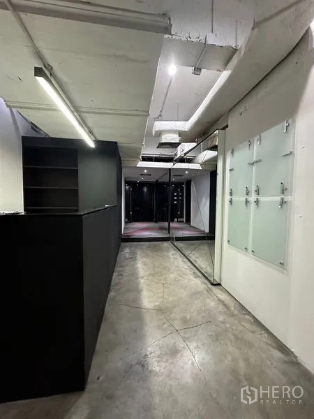 办公空间 出租在Watthana, Bangkok - 前台走廊，黑色接待台、镜面与玻璃门，混凝土地面。