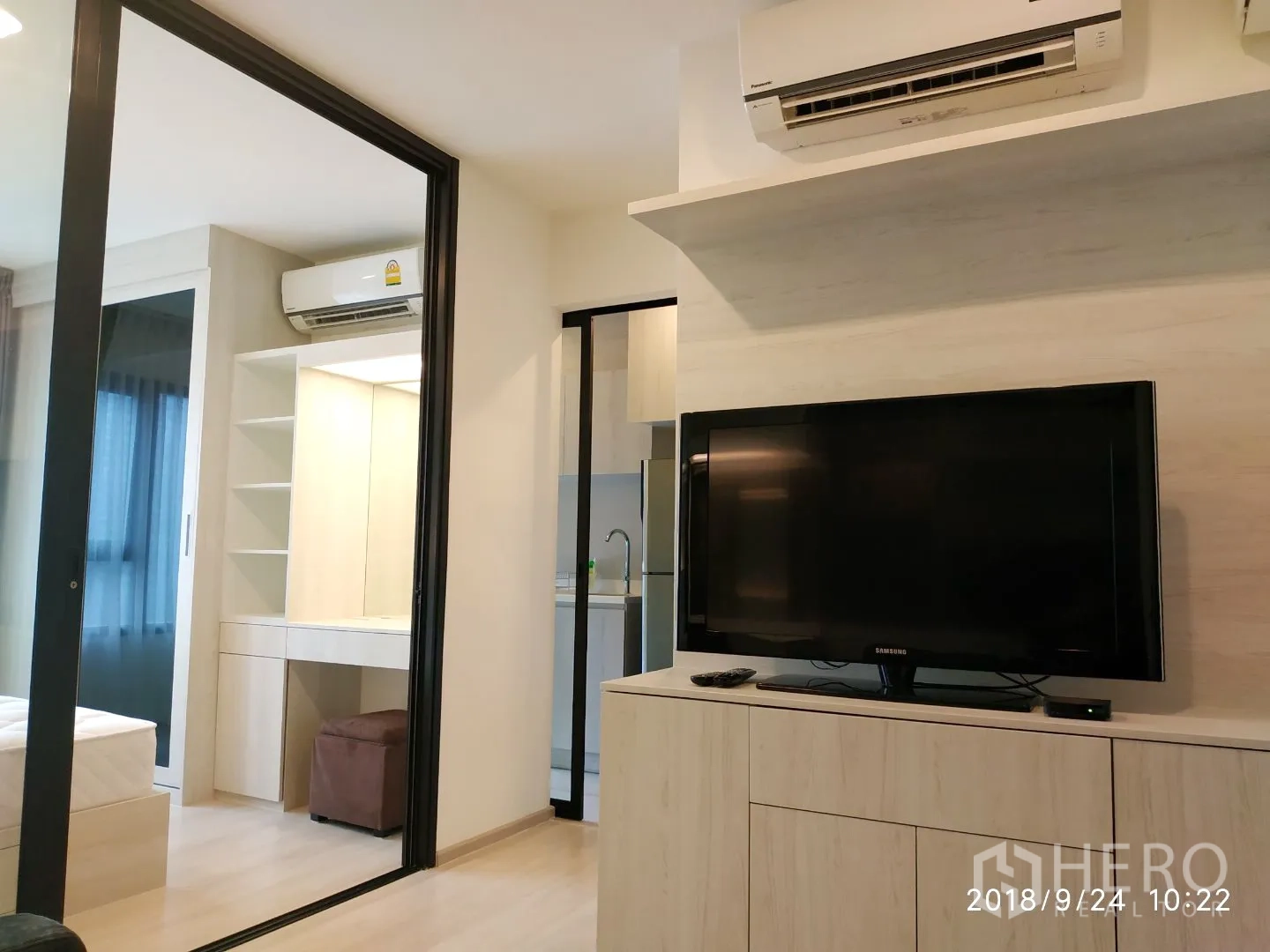คอนโด ให้เช่าในHuai Khwang, Bangkok - ห้องนั่งเล่นพร้อมชั้นวางทีวีและเครื่องปรับอากาศ เชื่อมต่อครัวและห้องนอนด้วยประตูกระจก.