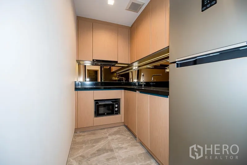 Condominium for rent in Watthana, Bangkok - Enclosed L‑shaped kitchen with wood cabinetry, black countertops and appliances.