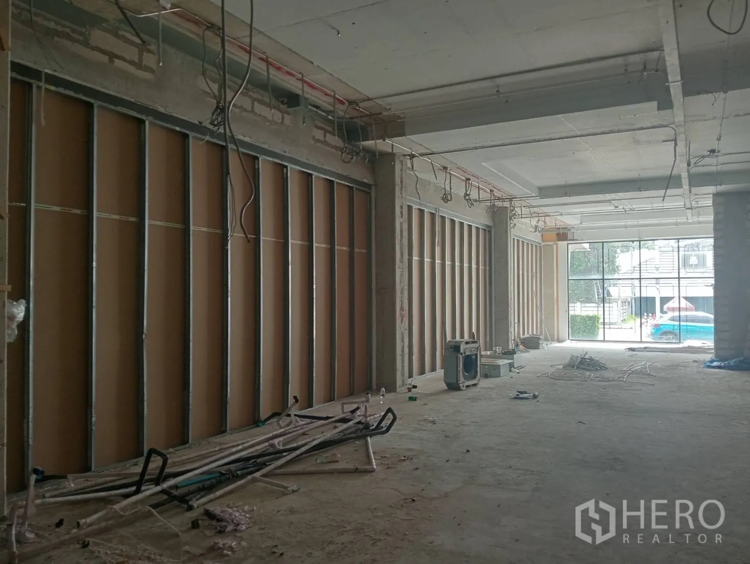 零售空间 出租 - 从店内望向玻璃门面与街景，墙体未完成、布线裸露。
