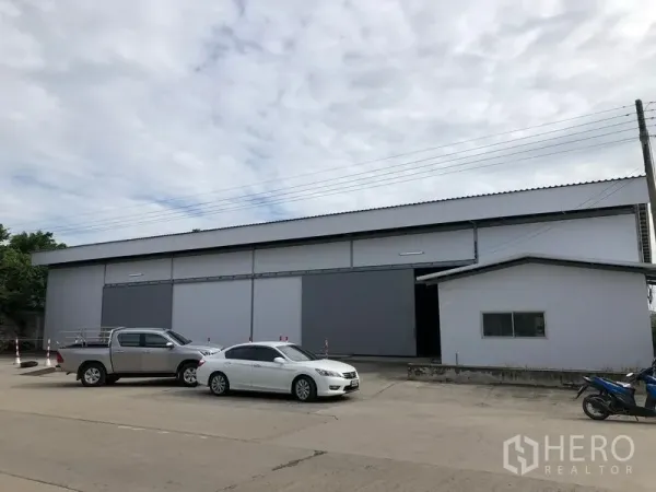 Warehouse for rent in Khlong Luang, Pathum Thani - Front exterior of a modern warehouse with large sliding doors and a wide driveway with parking space.