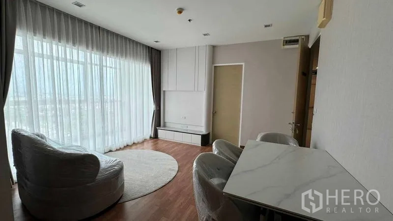 公寓 出租在Bang Na, Bangkok - 带大面积玻璃窗的客厅，圆形地毯、电视柜与大理石餐桌，木地板舒适温暖。