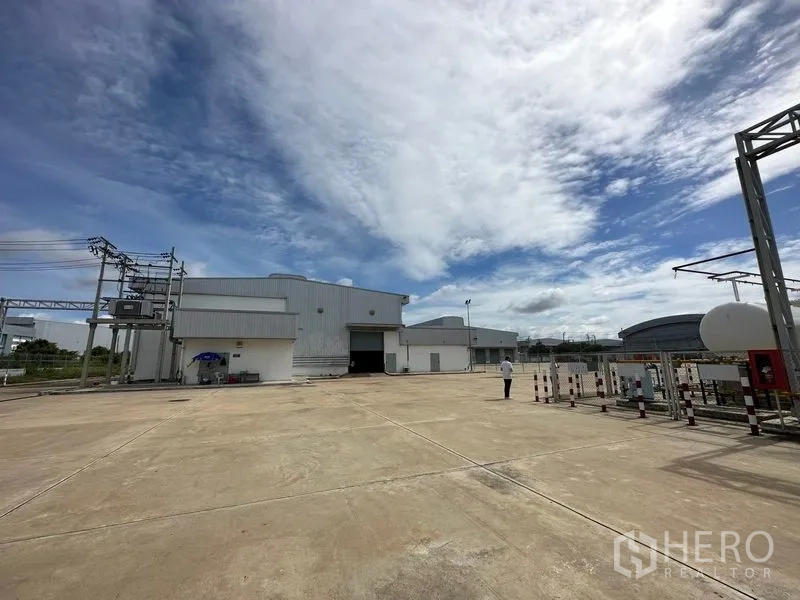 Factory for rent in Bang Sao Thong, Samut Prakan - Open concrete yard with utilities and factory buildings, ideal for truck maneuvering.