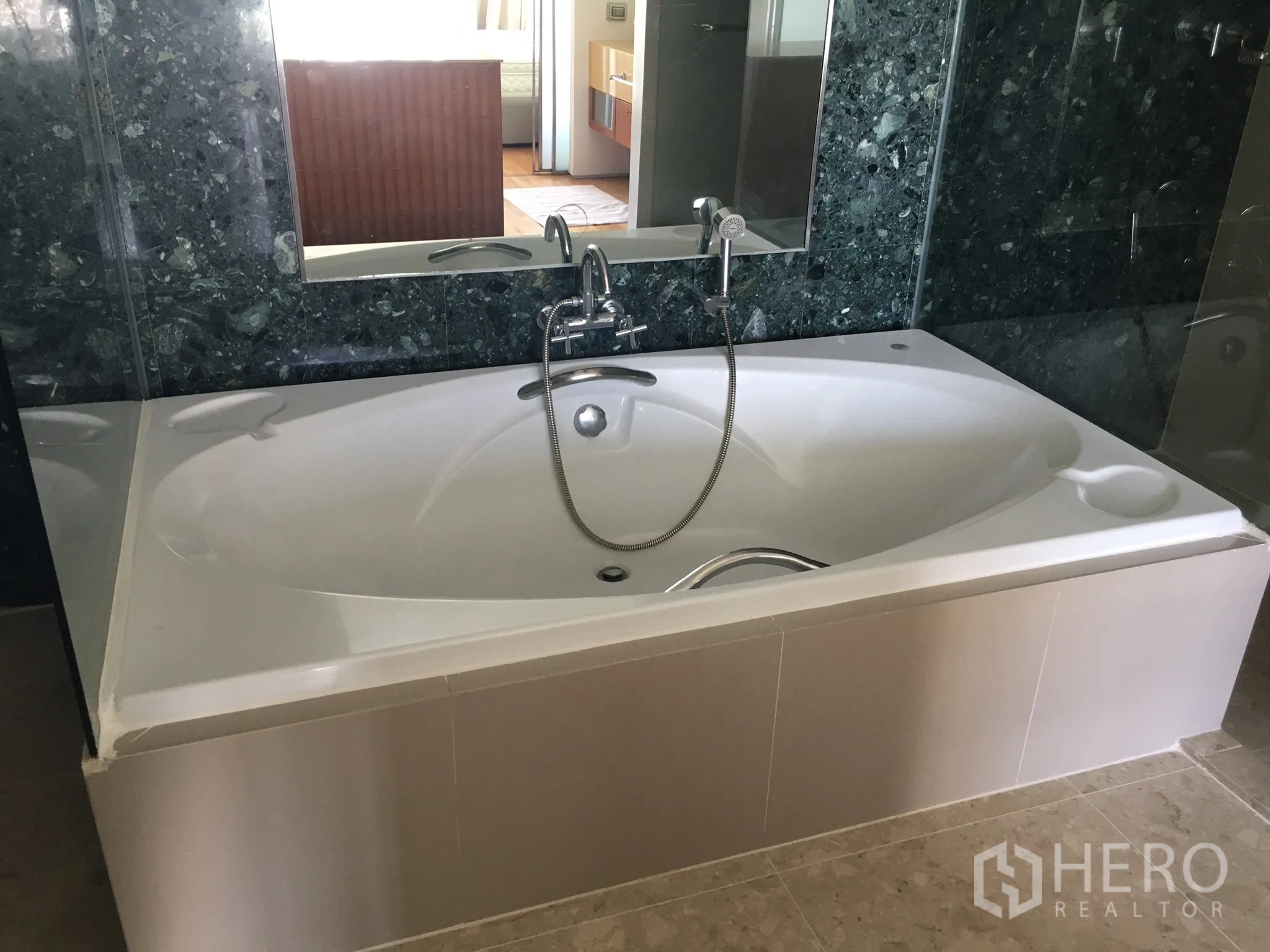 Condominium for rent in Khlong Toei, Bangkok - Spacious white soaking bathtub set against a dark marble wall.