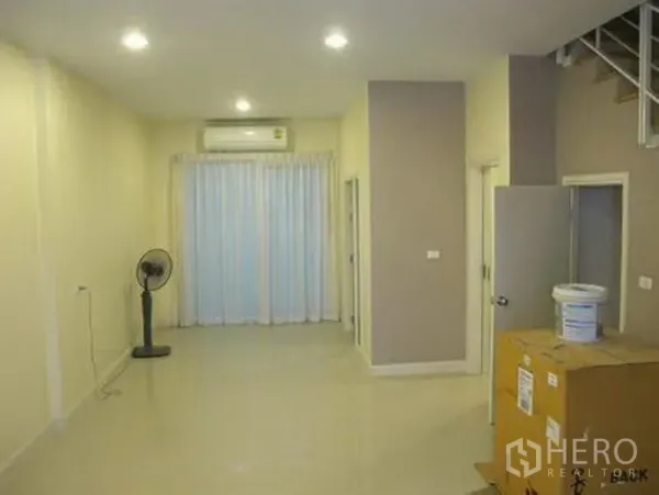 联排别墅 出租或出售在Wang Thonglang, Bangkok - 明亮客厅，亮面瓷砖地、筒灯、壁挂空调与落地窗帘。