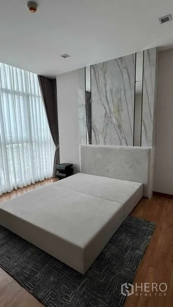 公寓 出租在Bang Na, Bangkok - 主卧配大理石质感背景墙、软包床架与角窗地毯，空间雅致。