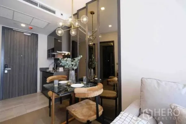 公寓 出租在Watthana, Bangkok - 大理石餐桌、吊灯与镜面装饰的用餐区，旁边是小厨房和入户门